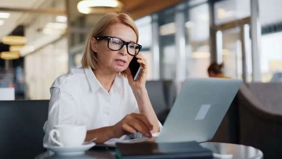 Smiling businesswoman on phone call, working on laptop in sleek office setting.